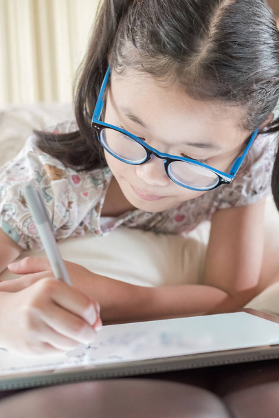 Азиатская школьница в очках с помощью планшетного устройства рисует на поверхности сенсорного экрана  - Фото, изображение
