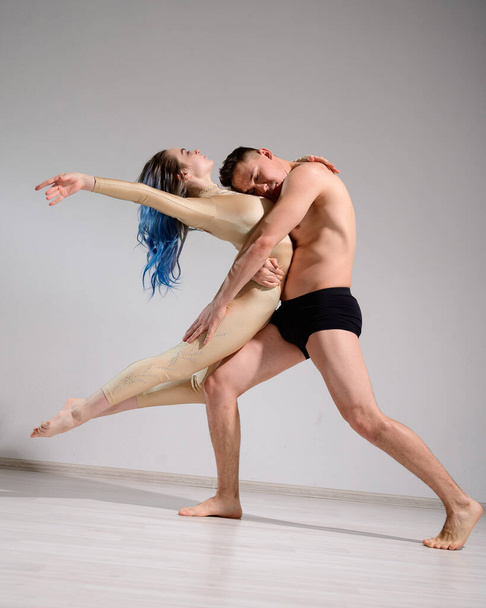 Acrobatic couple perform number on a white background. A duet of gymnasts rehearsing a performance with support. A man and a very flexible woman are dancing. - Φωτογραφία, εικόνα