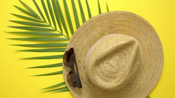 Slaměný klobouk, zelený palmový list a sluneční brýle na žlutém pozadí. Letní koncept. Byt ležel, horní pohled - Záběry, video