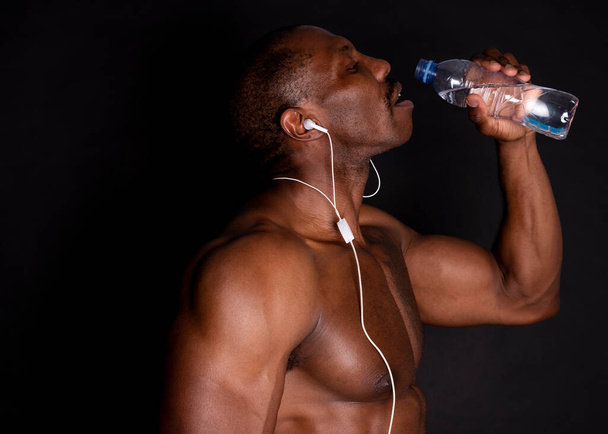 fitness man listens to music and drinks water, black background - Foto, immagini