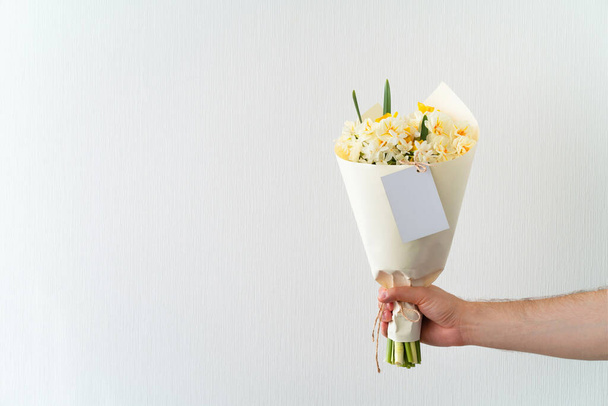 Man hand holding bouquet of white and yellow daffodils on white background. Copy space for text. - Zdjęcie, obraz