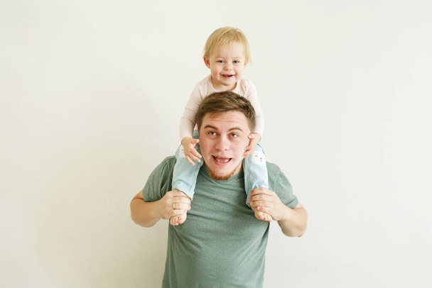 Young handsome father holding cute baby daughter kid on shoulders over light neutral background, laughing and having fun, father`s day holiday concept, stay home routine - Photo, image