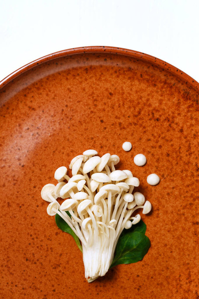 Enoki, Enokitake, Flammulina velutipes, edible mushroom popular in Japanese cuisine. Heap of little white mushrooms served on ceramics plate on white, dieting, close-up top view. - Foto, Imagem