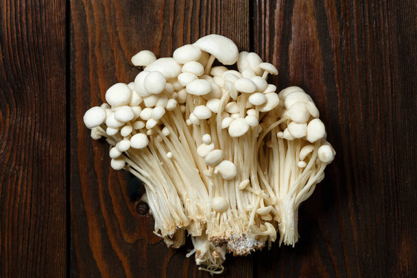 Enoki,  Enokitake, Flammulina velutipes, edible mushroom popular in Japanese cuisine. Heap of little white mushrooms served on wooden brown background. - Foto, afbeelding