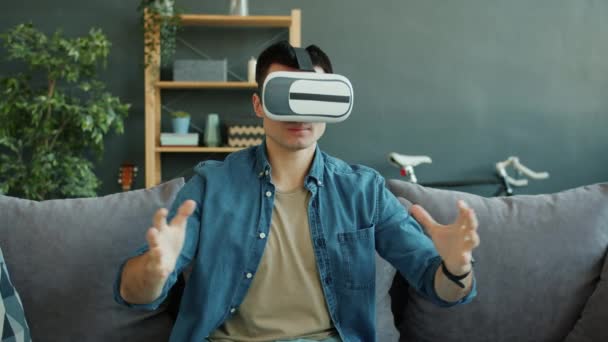 Slow motion of happy guy enjoying virtual reality glasses moving arms in apartment - Video, Çekim