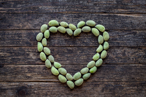 Muitas amêndoas verdes e secas na mesa com forma de coração. Conceito de alimentação saudável com amêndoas naturais
. - Foto, Imagem