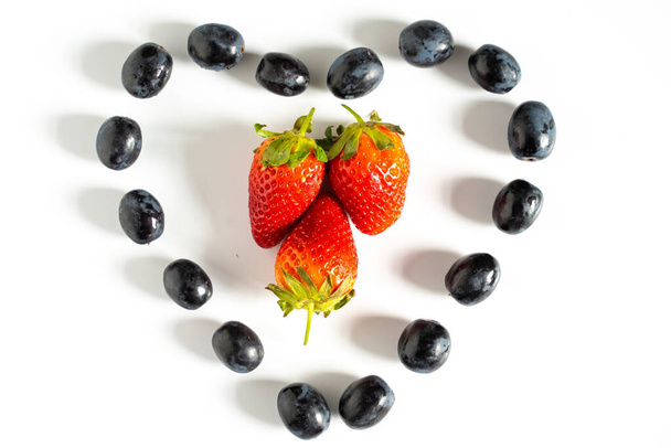 Trzy truskawki w środku wzoru kształtu serca czarnych winogron - Zdjęcie, obraz