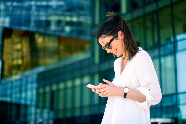 Shot of happy businesswoman text messaging while standing on the street. - Photo, Image