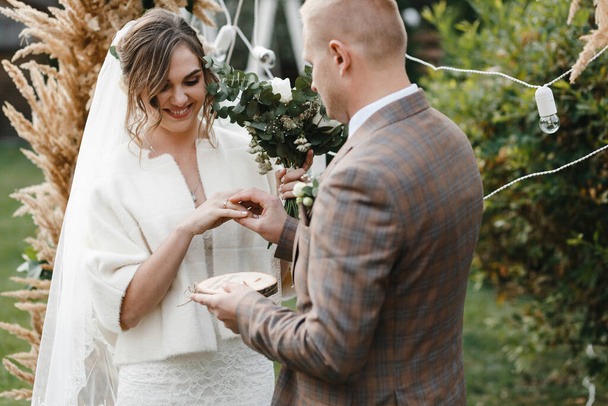 Der Bräutigam legt den Ehering auf den Finger der Braut. Braut und Bräutigam. Trauung. Trauung im Freien - Foto, Bild