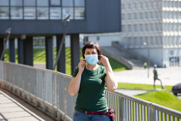 Пандемия коронавируса COVID-19. Женщина перед современным зданием носит защитную маску для распространения вируса SARS-CoV-2. Женщина в защитной маске на лице от коронавирусной болезни
. - Фото, изображение