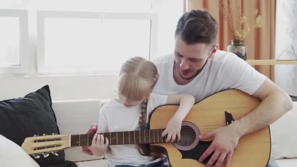 Young father teaches daughter to play the guitar at home - Imágenes, Vídeo