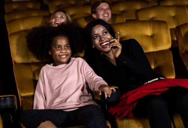 Nainen nauttii katsella elokuvaa tyttärensä kanssa elokuvateatterissa hymyillen ja nauraen yhdessä - Valokuva, kuva