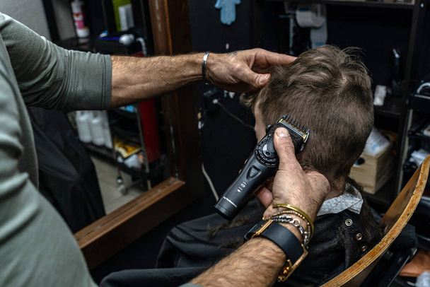 Berber, havalı bir berber dükkanında çocuğun saçını elektrikli makasla kesiyor. - Fotoğraf, Görsel