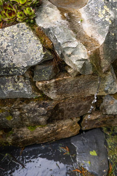 природный источник холодной и чистой родниковой воды между камнями и шифер
 - Фото, изображение