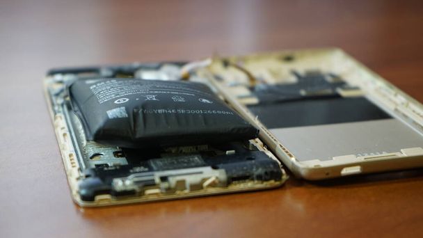 Swollen smartphone battery. Damaged smartphone with a faulty battery. Damaged phone on a wooden background. - Foto, Imagem