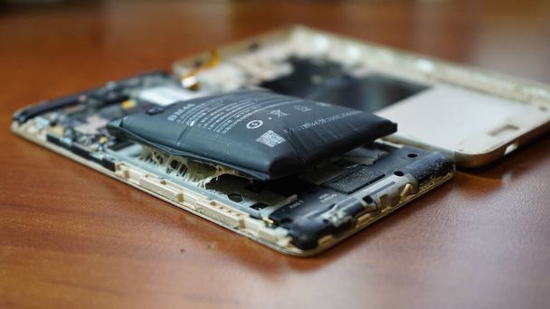 Opuchnięta bateria smartfona. Uszkodzony smartfon z wadliwą baterią. Uszkodzony telefon na drewnianym tle. - Zdjęcie, obraz