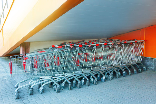Süpermarketin yakınındaki bir otoparkta merdivenlerin altında duran bir sürü metal alışveriş arabası var. - Fotoğraf, Görsel