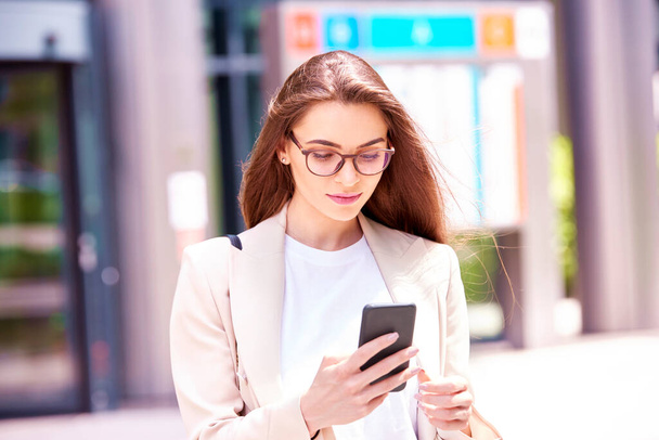 Close-up shot of young businesswoman standing on the street and text messaging.  - Фото, изображение