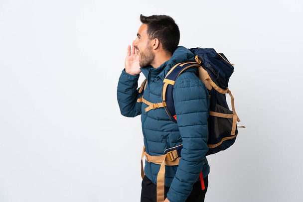 Młody alpinista z dużym plecakiem odizolowany na białym tle krzyczy z szeroko otwartymi ustami - Zdjęcie, obraz