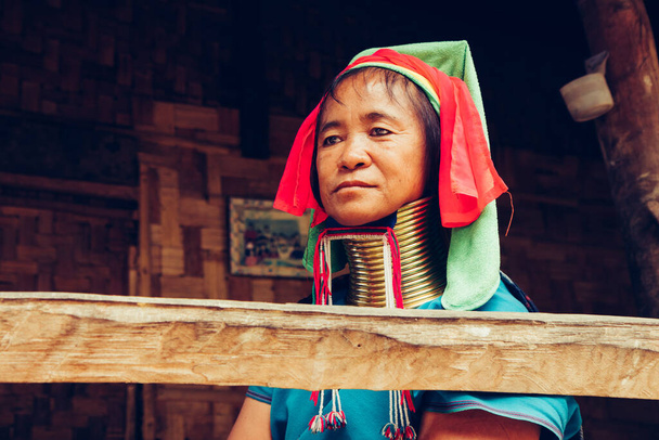Portret kobiety z długimi szyjami tkactwo przed jej domem w wiosce plemiennej Północnej Tajlandii. - Zdjęcie, obraz