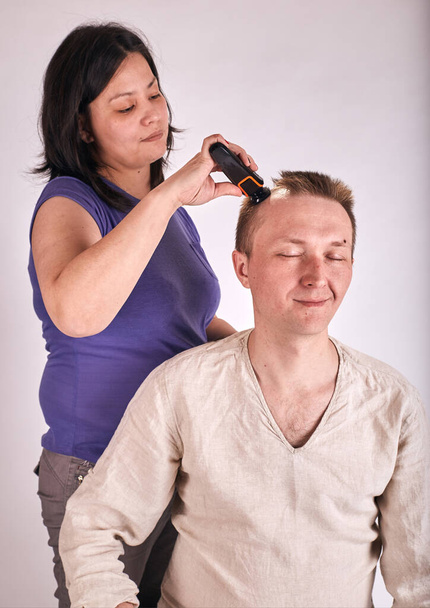 Ehefrau beim Haarschnitt für Ehemann zu Hause während Covid-19 Quarantäne. Selbstisolierter familiärer Lebensstil. - Foto, Bild