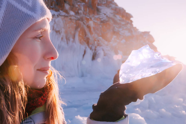 太陽の下で氷の塊を持つ旅の女性。ロシアの冬の観光バイカル湖。海岸沿いの冬の氷. - 写真・画像