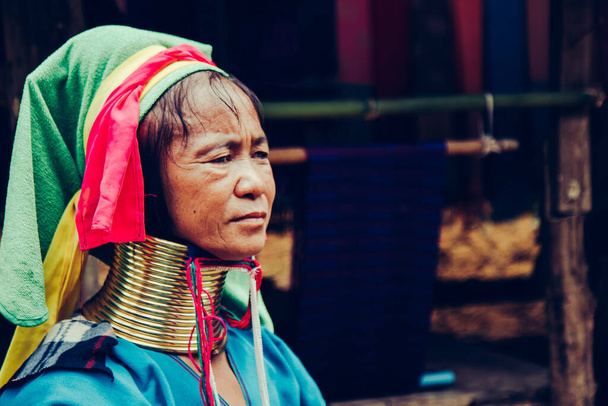 Porträt einer Frau mit langem Hals, die vor ihrem Haus in einem Stammesdorf in Nordthailand Stoffe webt. - Foto, Bild