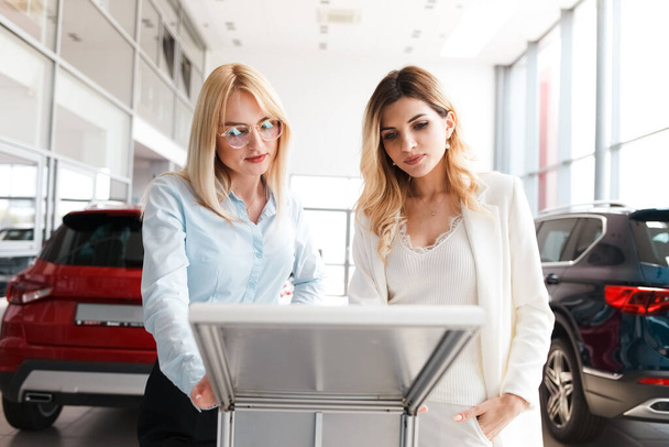 Verkäuferin zeigt einer jungen Frau eine Beschreibung eines Autos. Geschäftsfrau entscheidet sich für ein neues Auto - Foto, Bild