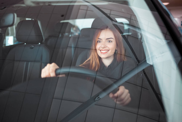 Smiling woman sitting at a car in a showroom - Foto, afbeelding