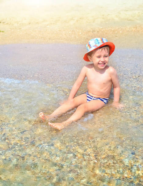 un niño feliz está sentado en el agua en la playa y salpicando en las olas. Un niño disfruta del mar
 - Foto, imagen