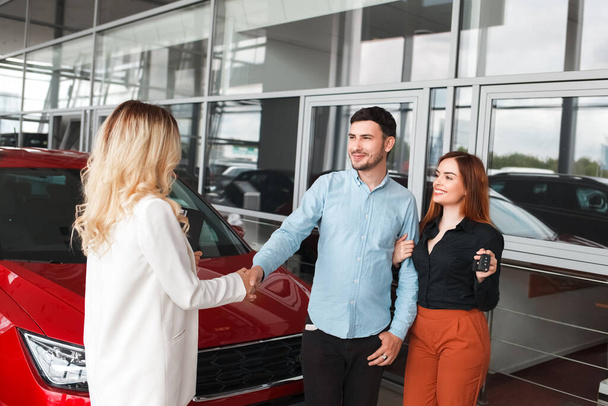Family couple at car dealership. Husband shakes hands with a car dealer after a successful deal - Photo, Image
