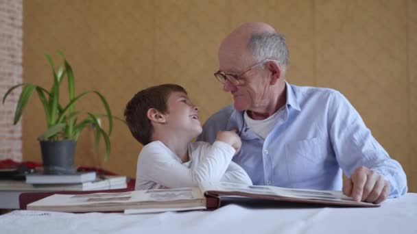 old elderly man in glasses for vision together with his grandson enjoy happy memories watching a family photo album - Footage, Video