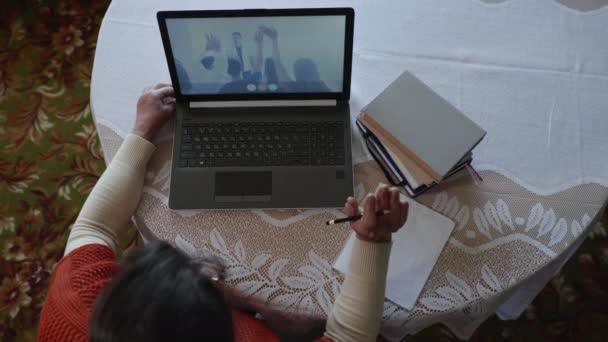 top view, oudere vrouw ondergaat verder onderwijs tijdens een online onderwijs, steekt de hand op en schrijft antwoord in notitieblok - Video
