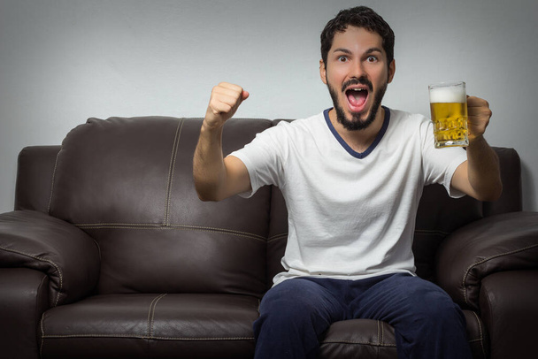 Sports, cheering concept - Enthusiastic man watching sports on tv and supporting team at home - Фото, зображення