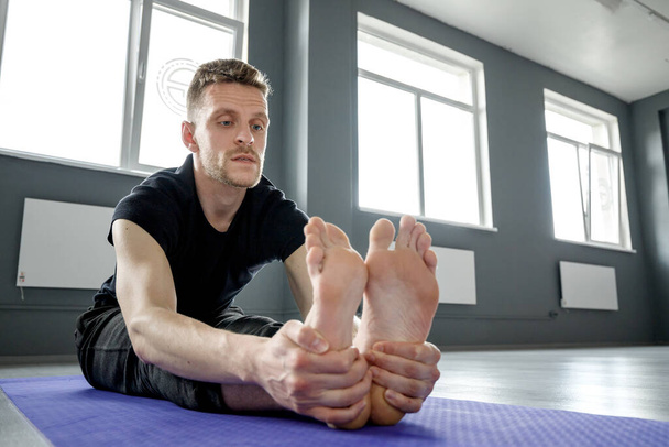 Jeune homme faisant des exercices d'étirement des jambes sur un tapis de yoga dans la salle de gym. Concentration sélective
. - Photo, image