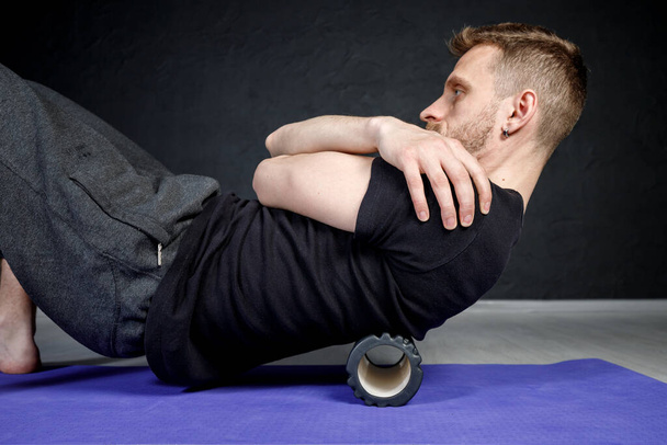 Young athletic man is working out his spine muscles with a roller. - Photo, Image
