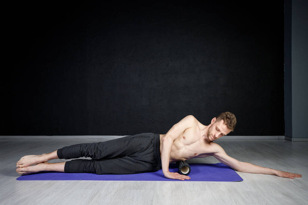 Young athletic man is working out his spine muscles with a roller. - Photo, Image