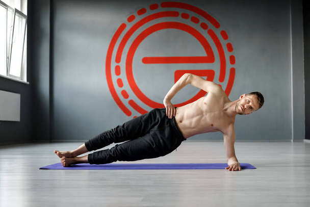Young, athletic man is doing exercise "Side forearm plank", with another arm on his waist. - Photo, Image