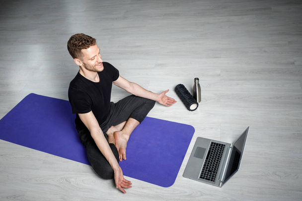 Молодой спортсмен медитирует перед ноутбуком. Уроки йоги онлайн
. - Фото, изображение