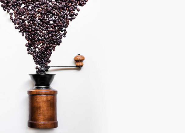 A lot of roasted black coffee beans dropping into retro wooden grinder on white background copy space on one side for commercial design work - Photo, image