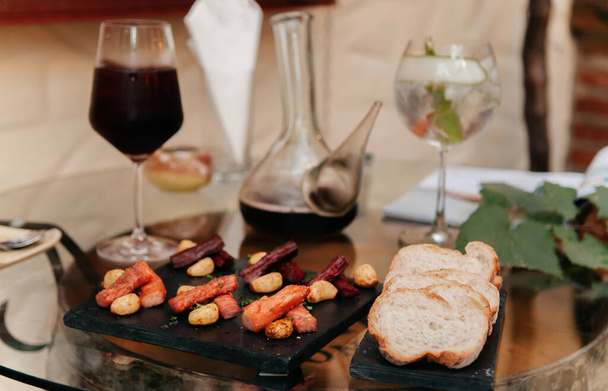 Κόκκινο κρασί και κοκτέιλ με ψωμί μπαγκέτας, αποξηραμένο βοδινό καπνιστό, ορεκτικό καναπεδάκι στο τραπέζι - Φωτογραφία, εικόνα