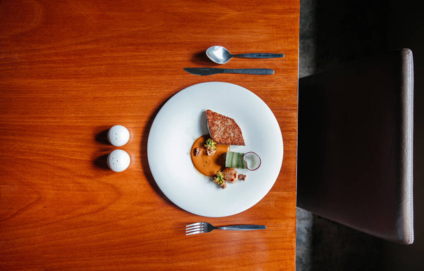 Seebarsch- und Jakobsmuschelsteak moderne Küche, gegrillter Seebarsch und Jakobsmuscheln mit Sahnesoße auf weißem Teller auf Holztisch, Aufnahme von oben - Foto, Bild