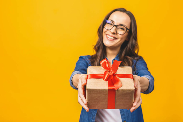 Happy brunetka kobieta w casual gospodarstwa prezent pudełko i patrząc w aparat podczas cieszy się na żółtym tle. - Zdjęcie, obraz
