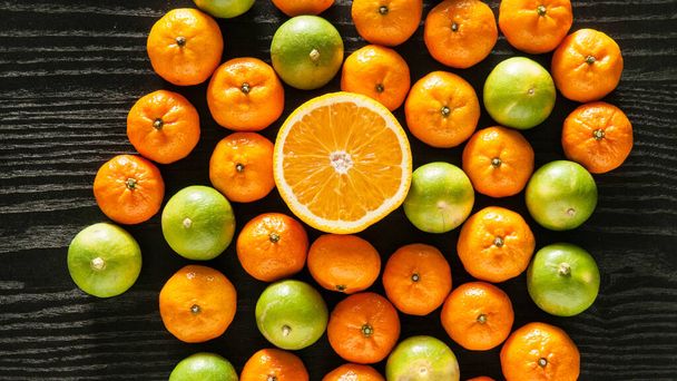 Frische volle Orangen, Limetten und halbierte Früchte auf schwarzem Holzhintergrund mit Kopierraum - Foto, Bild