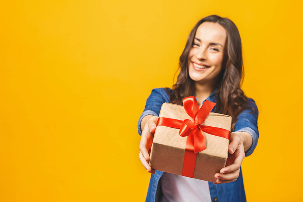 Uśmiechnięta młoda piękna kobieta trzyma czerwone pudełko z prezentami. Odizolowane na żółtym tle. Studio. - Zdjęcie, obraz