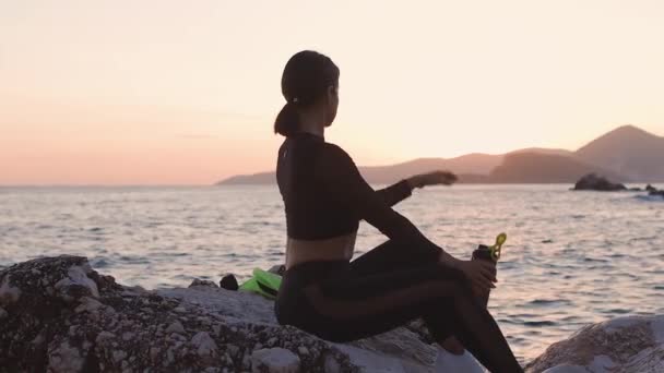 sportowa kobieta zrelaksować się na plaży pić białko shaker z widokiem na morze - Materiał filmowy, wideo