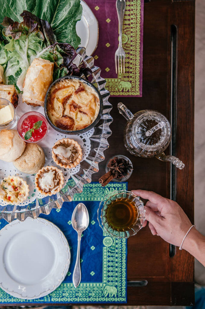 Élégance traditionnelle thé anglais de l'après-midi avec scone, tarte assortie et pâtisseries feuilletées sur une vieille table en bois, main tenant tasse de thé vue du dessus
 - Photo, image
