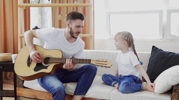Joven padre e hija familia feliz pasar tiempo juntos tocando la guitarra en sala de estar calidez fondo de la casa
. - Foto, imagen