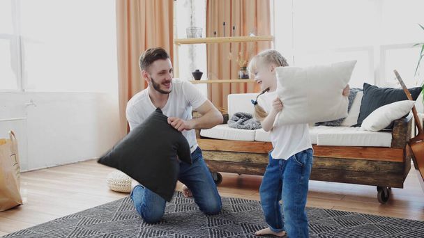 Father and daughter. Handsome young man and little cute girl play in pillow fight on the carpet at home, hug, have fun. Dad and child laugh. Father day - Foto, Bild