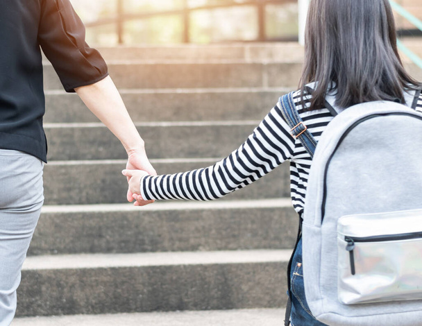Educational Back to school or bring kid to work concept with elementary student girl carrying backpacks holding parent woman or mother's hand walking up school office od admission building going to class - Photo, Image